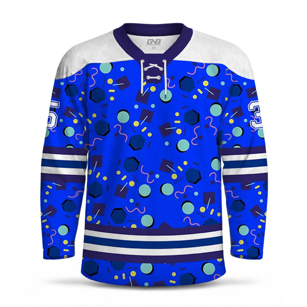 A long-sleeve hockey jersey with a royal blue body covered in a colorful abstract pattern of circles, hexagons, and wavy lines. It has a white shoulder yoke, dark purple collar and sleeve trim, white laces, and horizontal white and dark blue stripes near the hem.