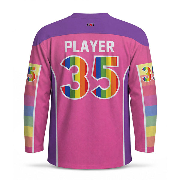 A long-sleeve hockey jersey shown from the back on a white background. The jersey is primarily pink with purple shoulder panels and rainbow-striped name and numbers on the back, plus matching rainbow accents on the sleeve numbers.