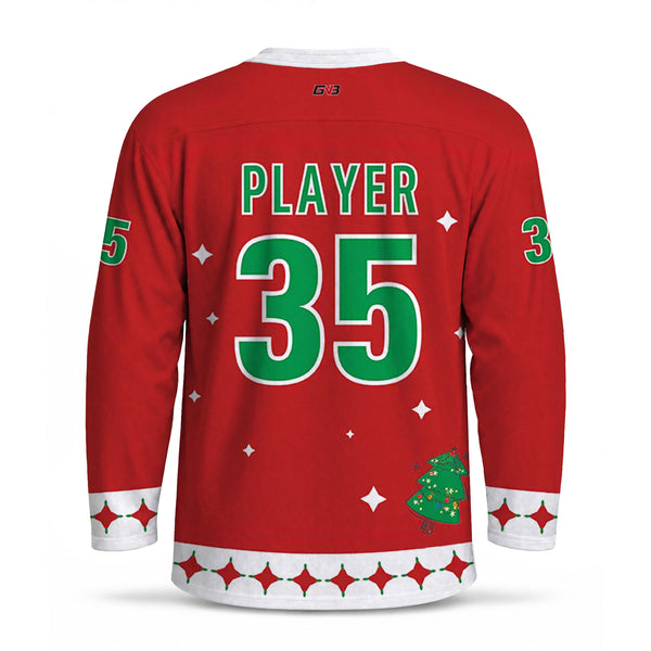 A red long-sleeve hockey jersey shown from the back, featuring 'PLAYER' and the number in green with white outlines. The bottom hem has a white patterned border with red star accents, and a small green Christmas tree graphic is near the lower right.