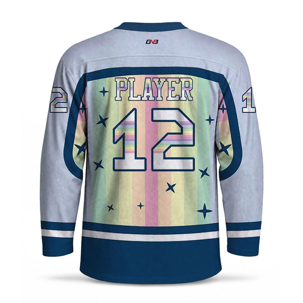 Back view of a long-sleeve hockey jersey. The jersey is light blue with navy blue trim and sleeves, featuring a large pastel rainbow-striped back panel with personalized name and large number and star motifs.
