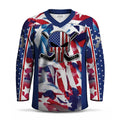 A long-sleeve hockey jersey with a patriotic red, white, and blue American flag star pattern, featuring a central skull graphic with crossed hockey sticks and a U.S flag.