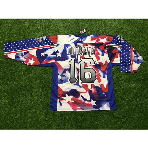 A hockey jersey laid flat on green artificial turf, featuring a patriotic red, white, and blue camouflage pattern with 'DURKIN' and the number '16' on the back.